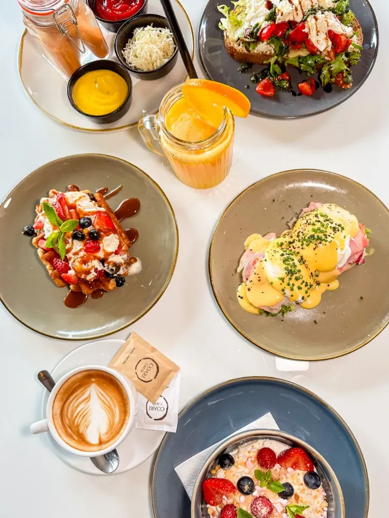 Breakfast table from above — waffle, eggs Benedict, granola and cappuccino