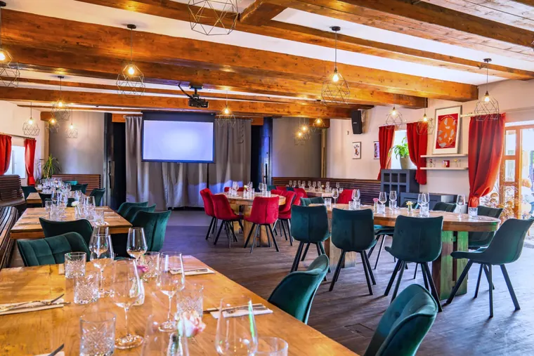 Café Cihelna events room set with long tables, beamed ceiling and projection screen