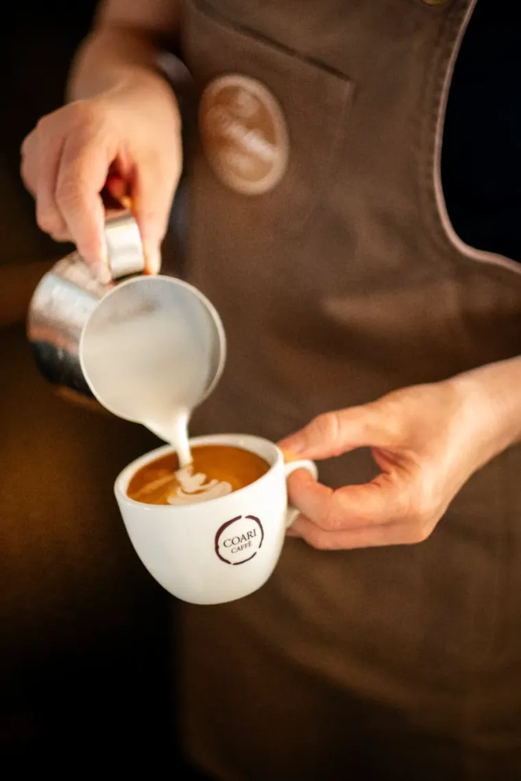 Barista pouring steamed milk into a fresh morning coffee